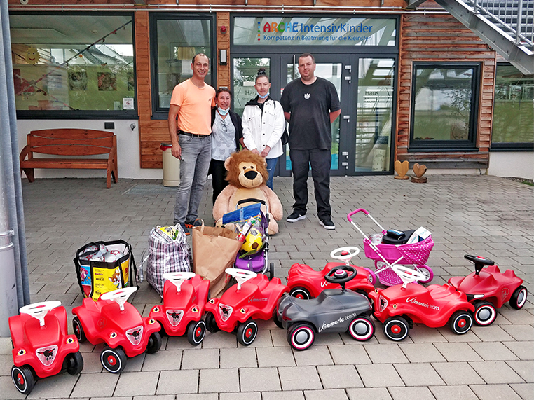 Das Bild zeigt die Spender Attila, Gülcan, Leonie und David hinter Taschen mit Spielsachen und Bobby Cars